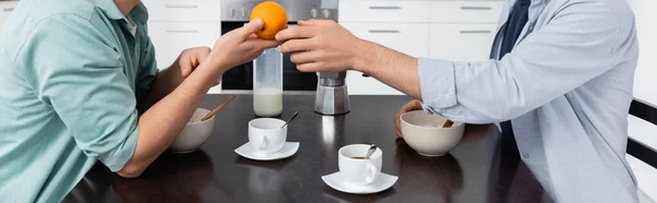 Vista recortada del hombre homosexual dando naranja al marido durante el desayuno, pancarta - foto de stock