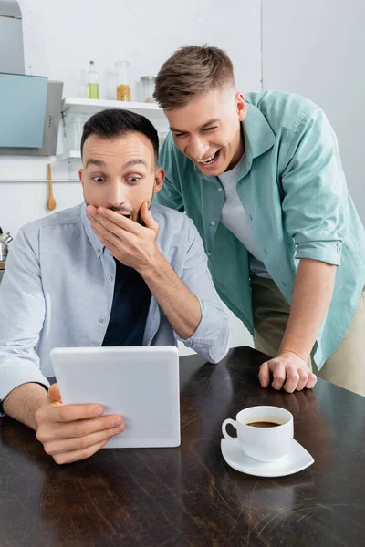 Étonné et joyeux couple de même sexe riant tout en regardant tablette numérique — Photo de stock