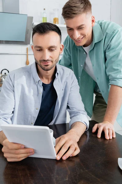 Gai même sexe couple souriant tout en regardant tablette numérique — Photo de stock