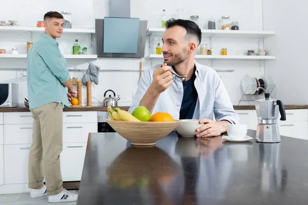 Feliz homosexual hombre comer maíz copos cerca marido en borrosa fondo - foto de stock