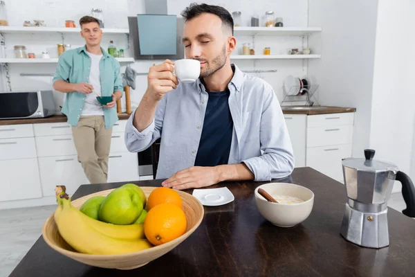 Homosexual hombre beber café cerca marido en borrosa fondo - foto de stock