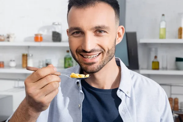 Hombre alegre y barbudo sosteniendo cuchara con hojuelas de maíz - foto de stock