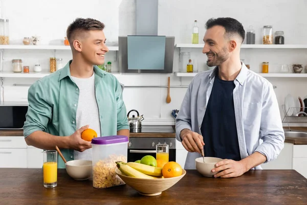 Glückliches gleichgeschlechtliches Paar, das sich in der Nähe von leckerem Frühstück auf dem Tisch anschaut — Stockfoto