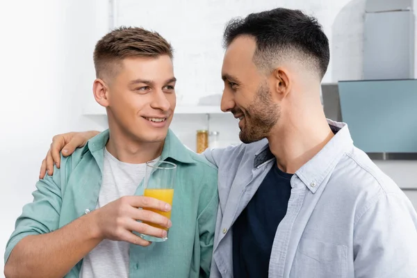 Hombre feliz sosteniendo vaso con jugo de naranja cerca de marido - foto de stock