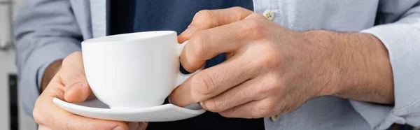 Обрезанный вид человека, держащего чашку с кофе и блюдцем, баннер — стоковое фото