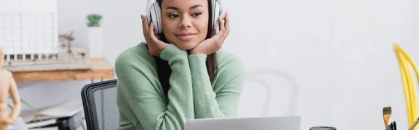 Alegre diseñador de interiores afroamericano escuchando música en auriculares en casa, pancarta - foto de stock