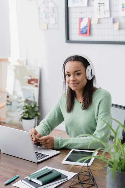 African american interior designer in headphones smiling at camera at workplace — Stock Photo