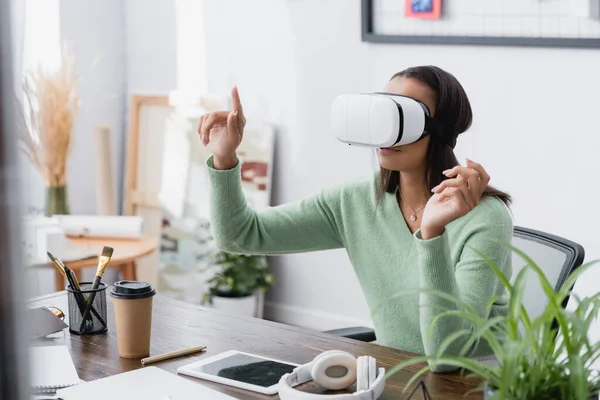 Africano americano independiente arquitecto gesto mientras se utiliza auriculares vr en el lugar de trabajo, borrosa primer plano - foto de stock