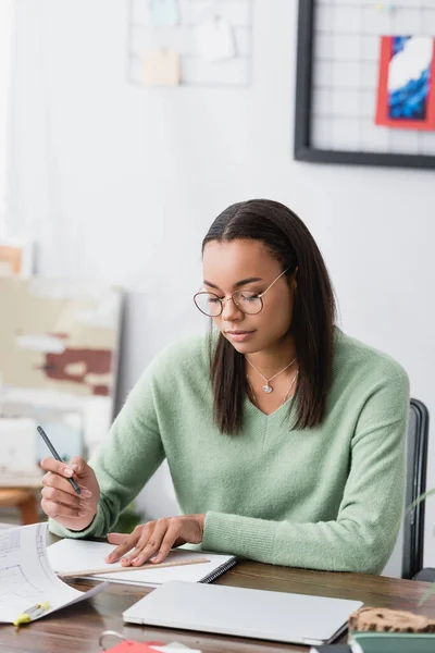 African american interior designer in eyeglasses drawing in sketchbook with pencil and ruler — Stock Photo