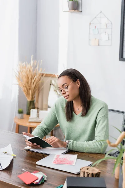 Young african american architect looking in notebook while sitting at work desk — Stock Photo