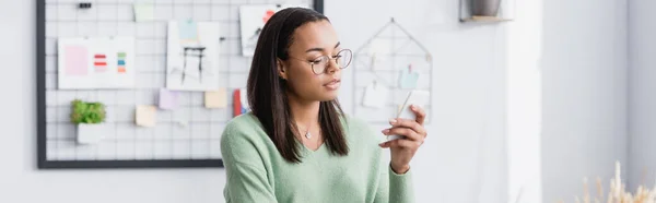 Young african american architect in eyeglasses messaging on smartphone, banner — Stock Photo