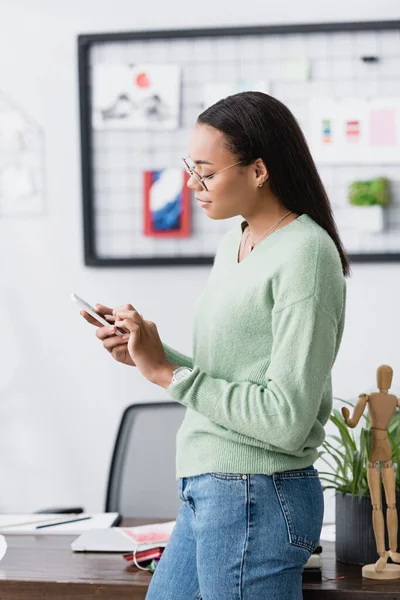 Side view of african american interior designer texting on cellphone at home — Stock Photo