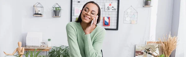 Feliz africano americano arquitecto sonriendo mientras habla en el teléfono móvil, bandera - foto de stock