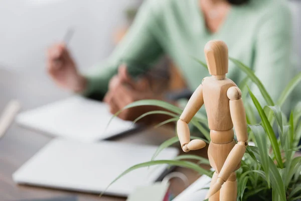 Selective focus of wooden human figurine and green plant near african american architect on blurred background — Stock Photo