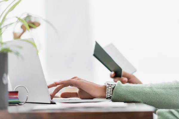 Partial view of african american freelancer typing on laptop while holding notebook on blurred foreground — Stock Photo