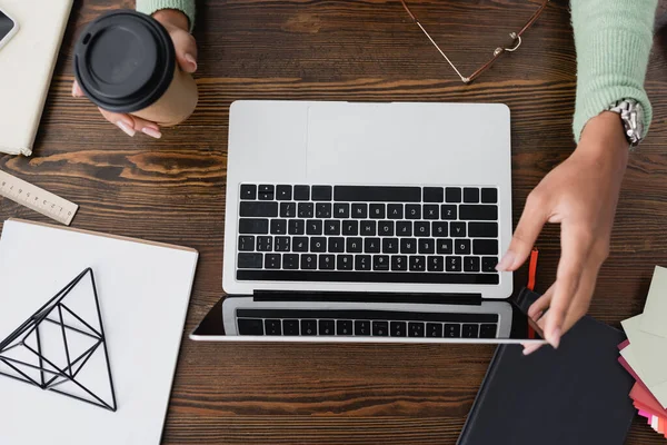 Vue recadrée de l'architecte afro-américain tenant du café pour aller près de l'ordinateur portable sur le bureau — Photo de stock