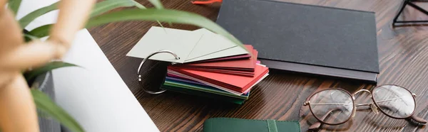 Eyeglasses near samples of material for interior decor near notebook on desk, blurred foreground, banner — Stock Photo
