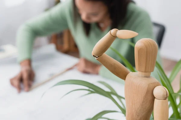 Foyer sélectif de figurine humaine en bois près de l'architecte afro-américain travaillant sur fond flou — Photo de stock