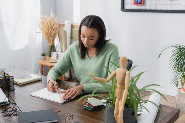 Joven arquitecto afroamericano dibujo en cuaderno de bocetos con regla y lápiz en el estudio en casa - foto de stock