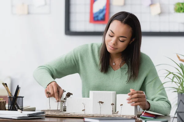 Arquitecto afroamericano positivo haciendo maqueta de edificios en el estudio en casa - foto de stock