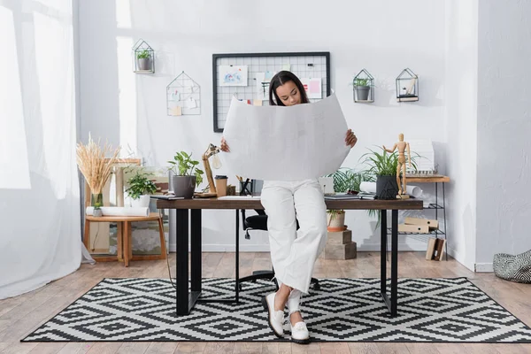 Arquitecto afroamericano celebración de proyecto mientras se apoya en el escritorio en el estudio en casa - foto de stock