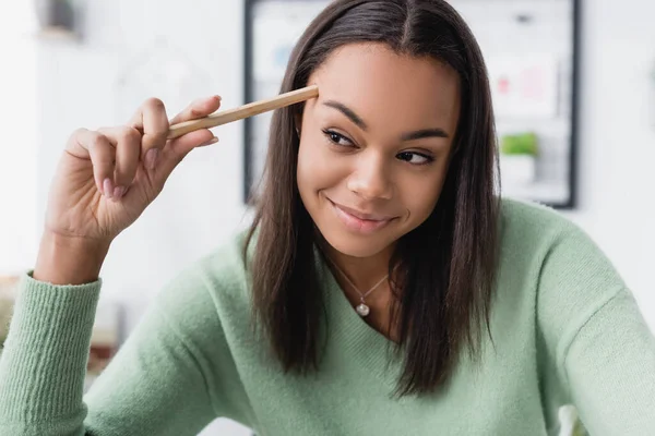 Happy african american interior designer touching head with pencil and looking away — Stock Photo