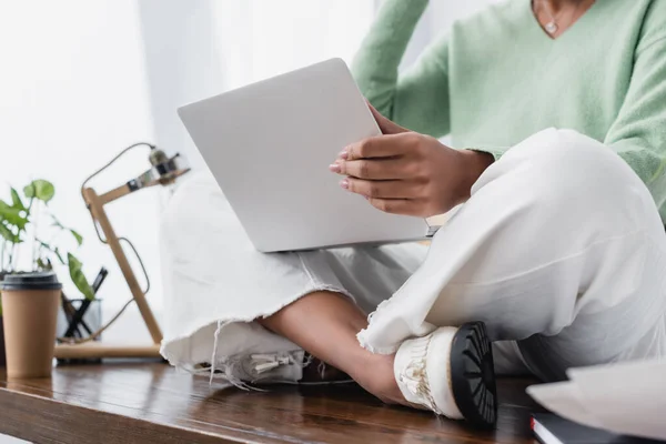 Vue recadrée de l'architecte afro-américain assis sur le bureau avec ordinateur portable, fond flou — Photo de stock