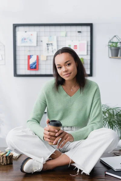 Young african american architect sitting on desk with coffee to go and looking at camera — Stock Photo
