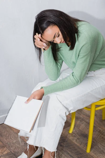Exhausted african american interior designer sitting on chair with blank sketchbook — Stock Photo