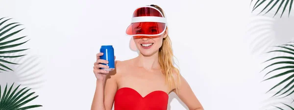 Mulher alegre no visor do sol sorrindo para a câmera enquanto segurando lata de refrigerante no branco, banner — Fotografia de Stock