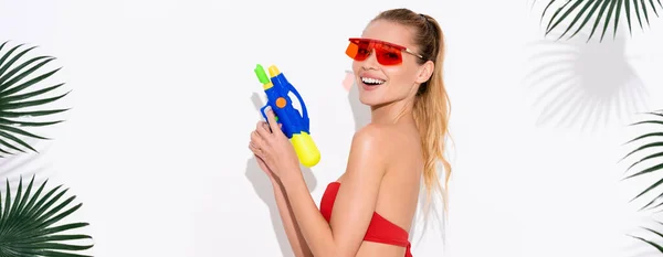 Excited woman looking at camera while posing with water gun on white, banner — Stock Photo