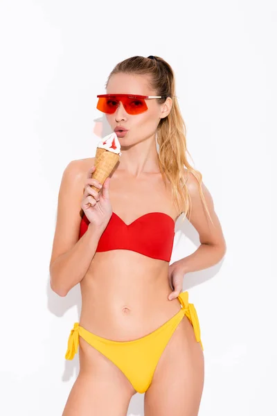 Young woman in swimsuit and sunglasses holding ice cream in waffle cone on white — Stock Photo