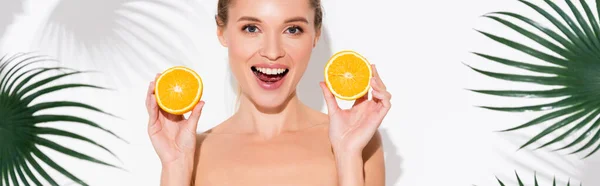 Изумленная женщина смотрит в камеру, держа половинки свежего апельсина на белом, баннер — стоковое фото