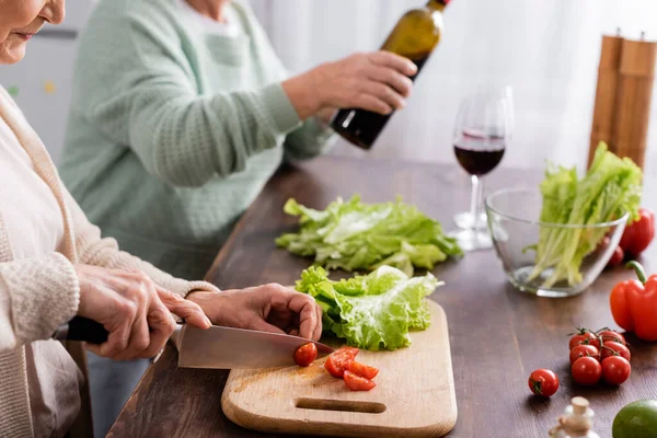 Vista ritagliata della donna in pensione taglio pomodoro ciliegia sul tagliere — Foto stock