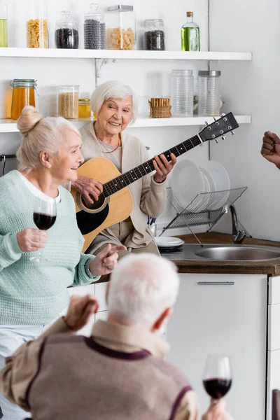 Glückliche Rentnerin spielt Akustikgitarre bei Freunden in der Küche — Stockfoto