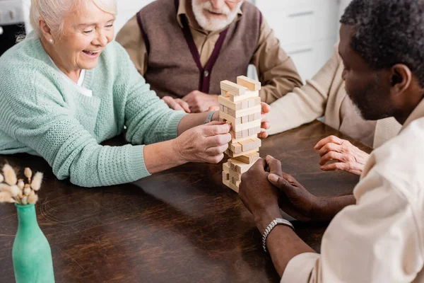 Felizes pensionistas multiculturais jogando torre blocos de madeira jogo em casa — Fotografia de Stock