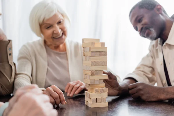 Tower wood blocks on table near happy multicultural pensioners on blurred background — Stock Photo