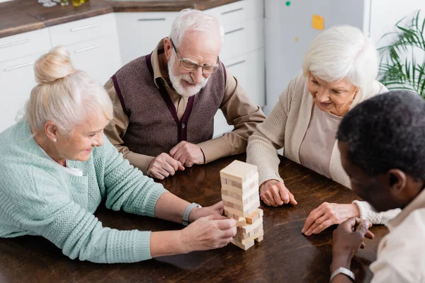Visão de alto ângulo de aposentados multiculturais felizes jogando torre blocos de madeira jogo em casa — Fotografia de Stock