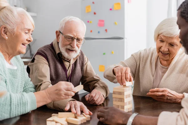 Happy interracial pensioners smiling while playing tower wood blocks game at home — Stock Photo
