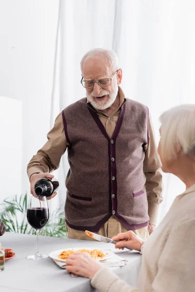 Старший чоловік в окулярах поливає червоне вино в келиху жінки у відставці — стокове фото
