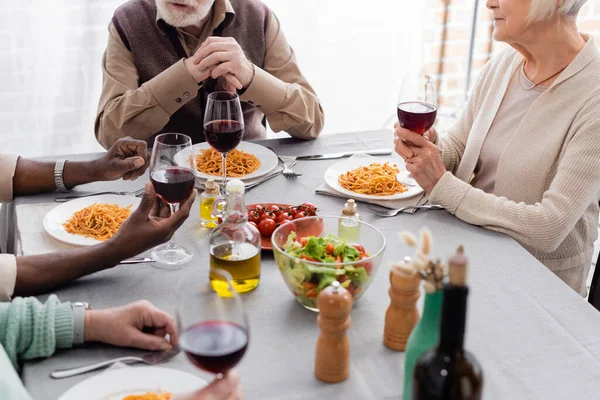 Vista cortada de amigos multiculturais e seniores tendo delicioso almoço juntos — Fotografia de Stock