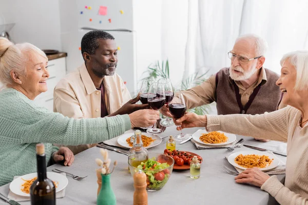 Happy multicultural pensioners clinking glasses of red wine during lunch — Stock Photo