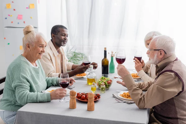 Fröhliche und pensionierte multikulturelle Freunde beim gemeinsamen Mittagessen — Stockfoto