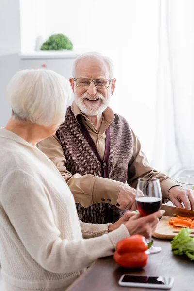 Happy senior man cutting bell pepper near wife with glass of wine — Stock Photo