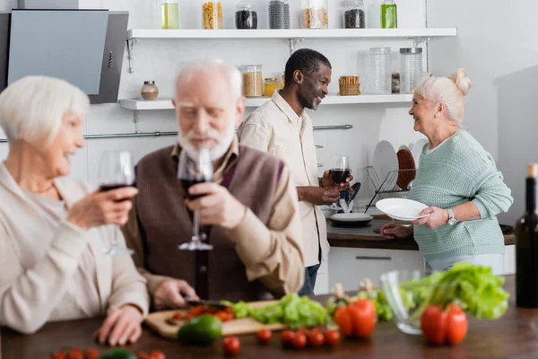 African american man and happy senior woman looking at each other near retired friends on blurred foreground — Stock Photo