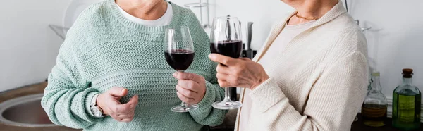 Частковий вид на пенсіонерів, що тримають келихи червоного вина, банер — стокове фото