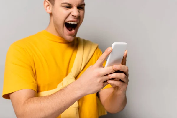 Smartphone in hands of angry man blurred on grey background — Stock Photo