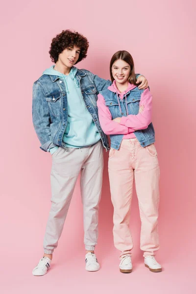 Smiling teenager hugging friend and looking at camera on pink background — Stock Photo