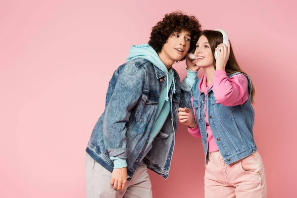 Adolescentes alegres escuchando música en auriculares sobre fondo rosa - foto de stock