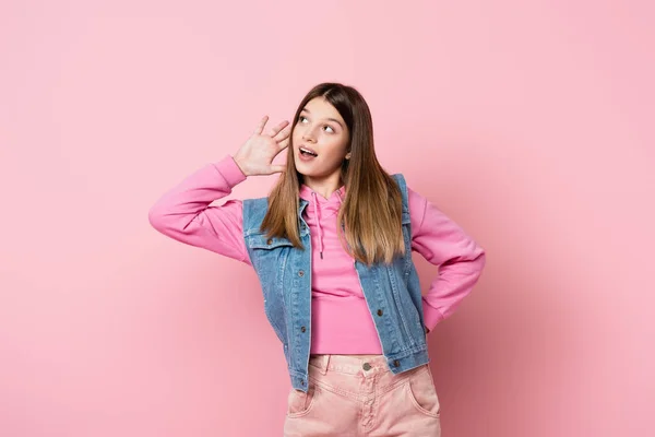 Adolescente con la mano cerca de la oreja mirando hacia otro lado sobre fondo rosa - foto de stock